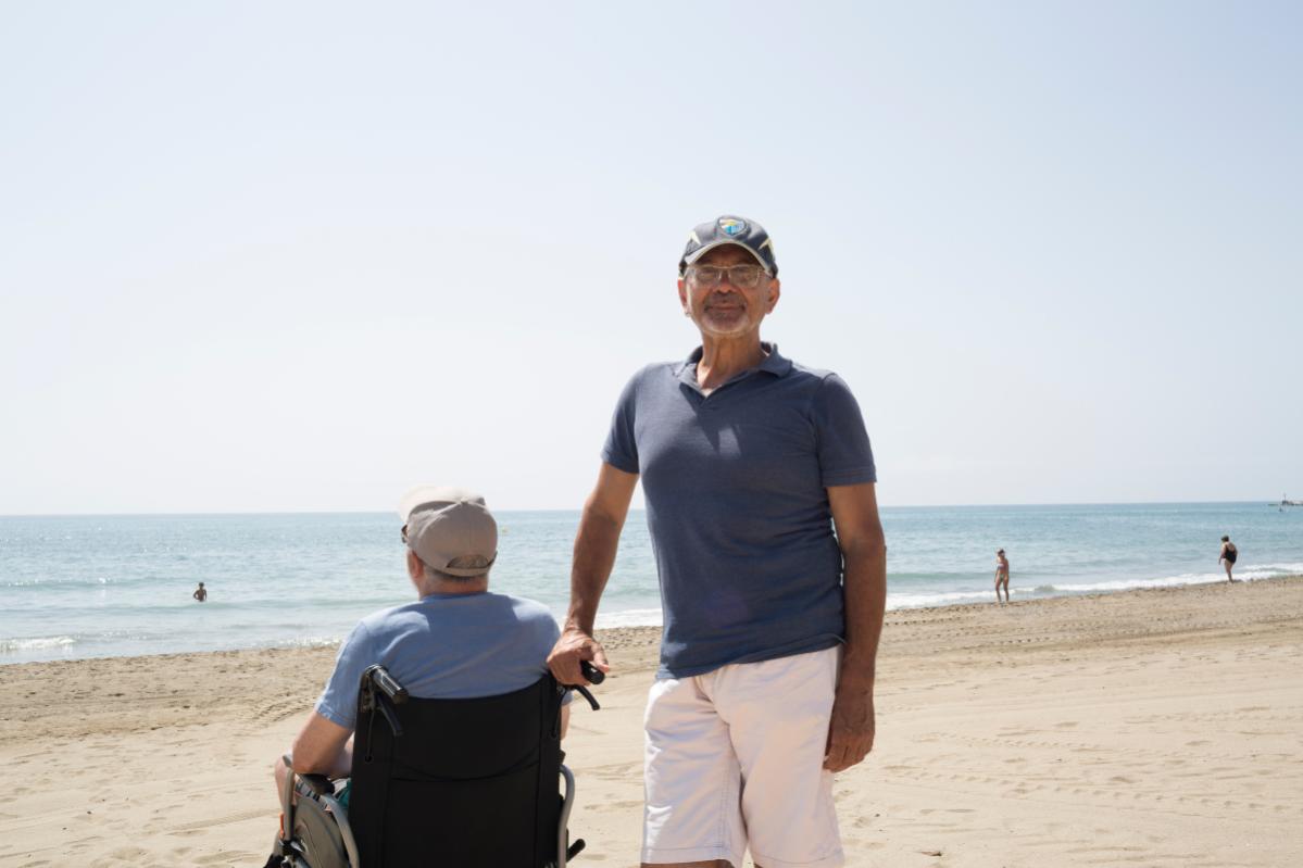 Francesco, beneficiario del programa Tarjetas Solidarias y participante de programas de Acción contra el Hambre para la mejora del empleo, en  la playa, junto a la persona anciana de la que cuida - Seguridad Alimentaria